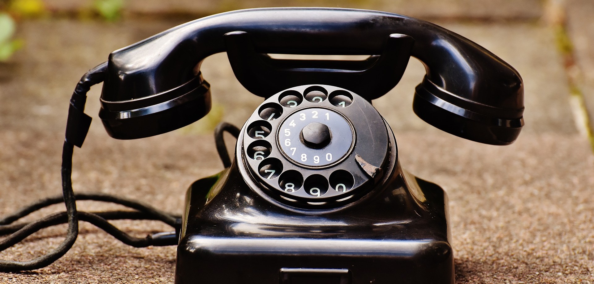 Ein sehr altes schwarzes Telefon mit Wählscheibe steht draußen auf einem Bürgersteig