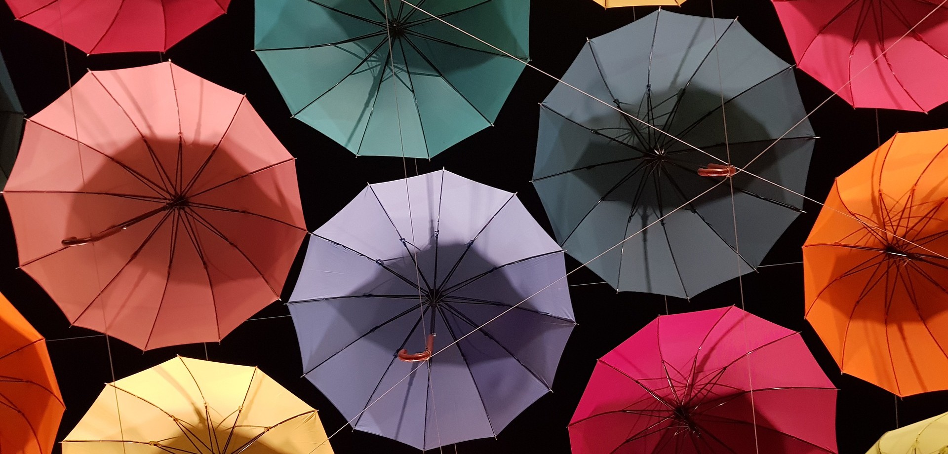 Mehrere bunte, verschiedenfarbige Regenschirme hängen geöffnet und miteinander verbunden oben an einer Wohnungsdecke