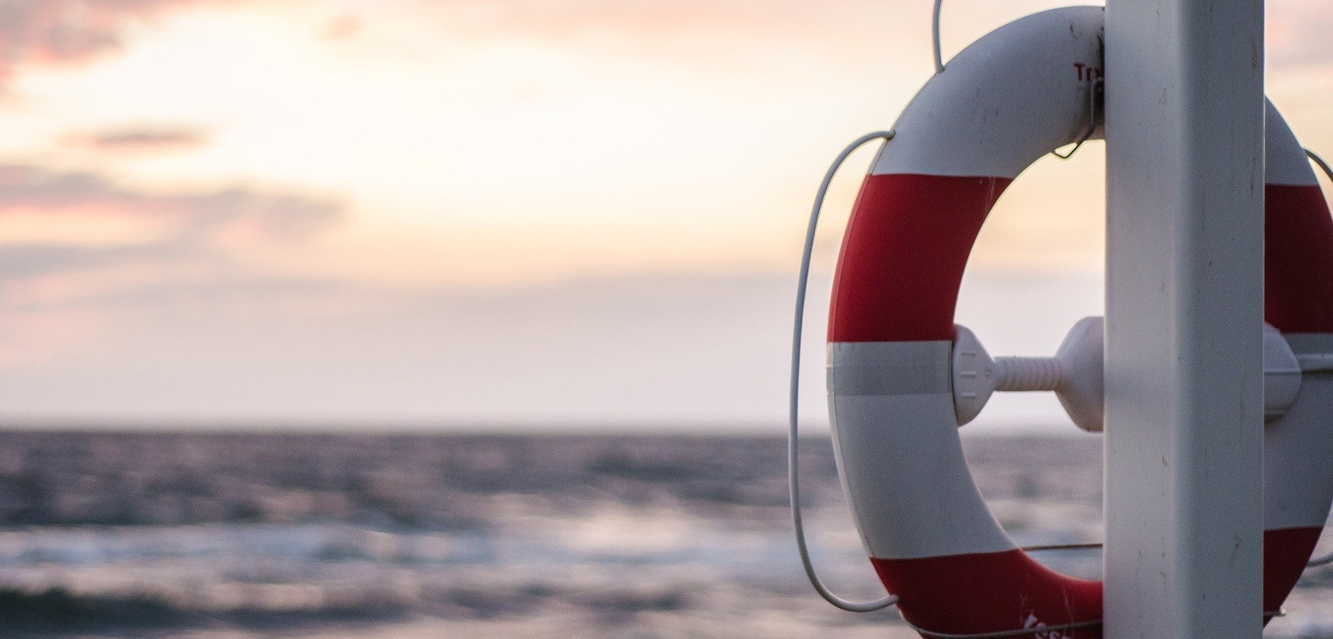 Ein Rettungsring hängt am Stand an einem weißen Metallpfosten, im Hintergrund schlägt das Meer Wellen